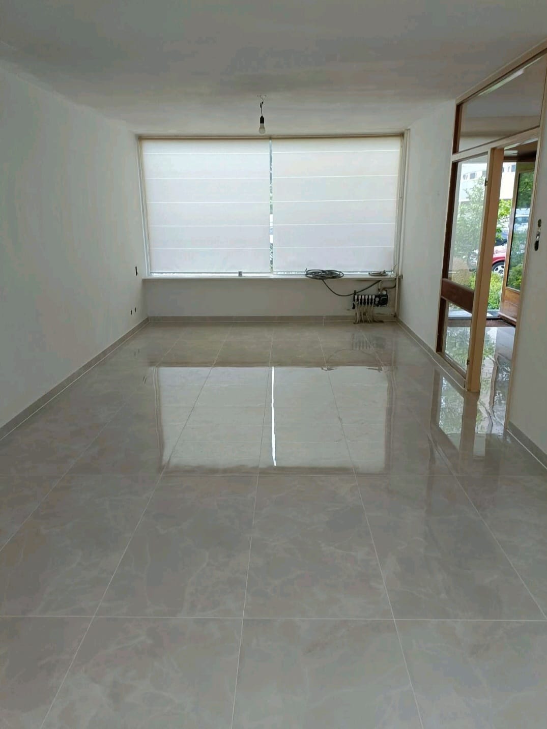 Woonkamer met een strak gelegde glanzende tegelvloer, afgewerkt na renovatie.